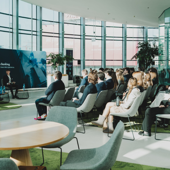 zdjecie pokazujące studentów na oszklonej sali i kilku prelegentów rozmawiających ze sobą podczas panelu dyskusyjnego
