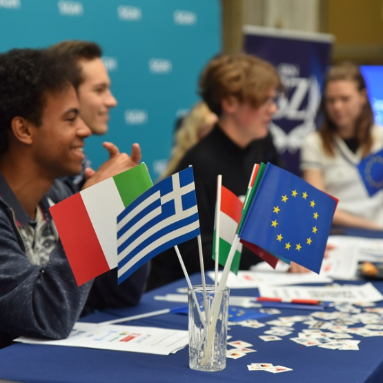 kilka osób siedzi za stołem; na pierwszym planie kilka flag, w tym flaga UE