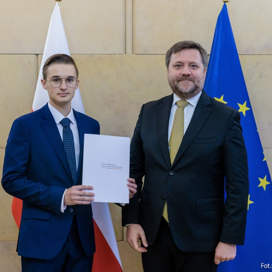 dwóch mężczyzn w garniturach na tle flagi Polski i UE