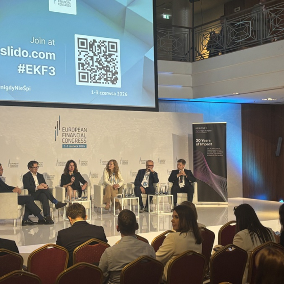 kilka osób dyskutuje na panelu, widać też ludzi siedzących na widowni