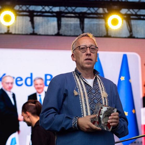 mężczyzna w ludowej koszuli trzyma statuetkę na scenie