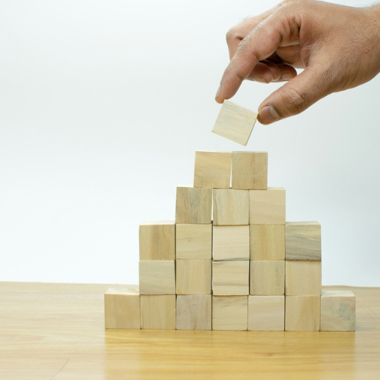 męska dłoń wyciąga jeden klocek z ułożonej piramidy 