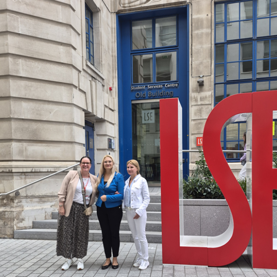 zdjęcie trzech kobiet przed siedzibą London School of Economics, kobiety stoją przy dużym akronimie LSE 