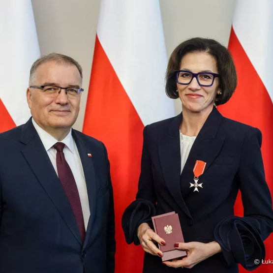 kobieta przyjmuje odznaczenie; zdjęcie na tle trzech polskich flag