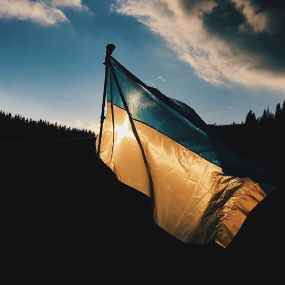 ukraińska flaga powiewająca na wietrze; w tle las i zachmurzone niebo