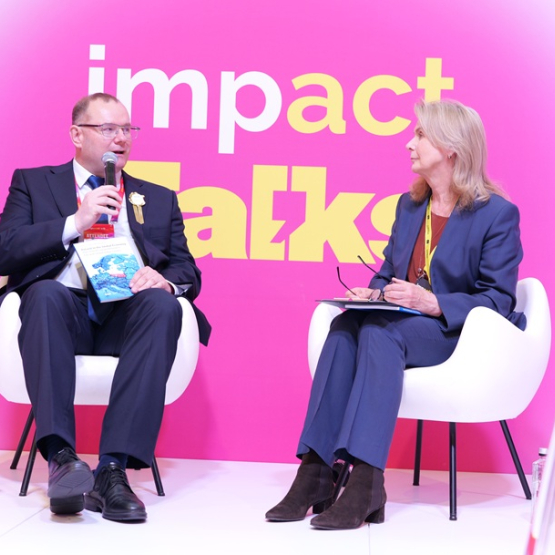 Kobieta i mężczyzna rozmawiają na panelu; w tle różowa ścianka