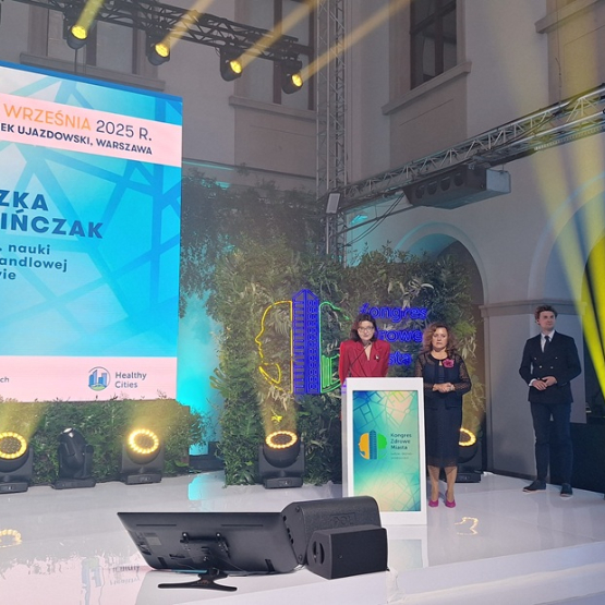 trzy osoby stoją na scenie, kobieta przemawia