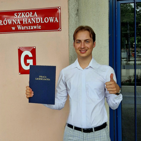 na zdjęciu Paweł Wróblewski z pracą dyplomową na tle budynku SGH