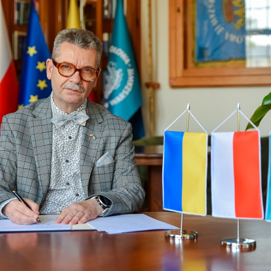 mężczyzna podpisuje dokumenty, obok proporczyki z flagą Ukrainy, Polski i SGH