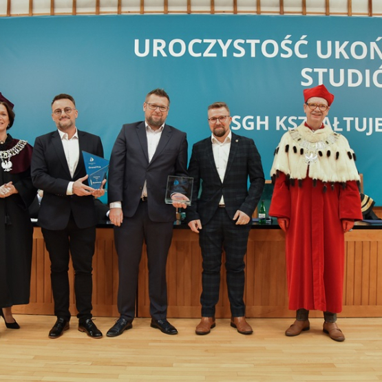 trzech mężczyzn w garniturach oraz kobieta i mężczyzna w togach rektorskich stoją na scenie