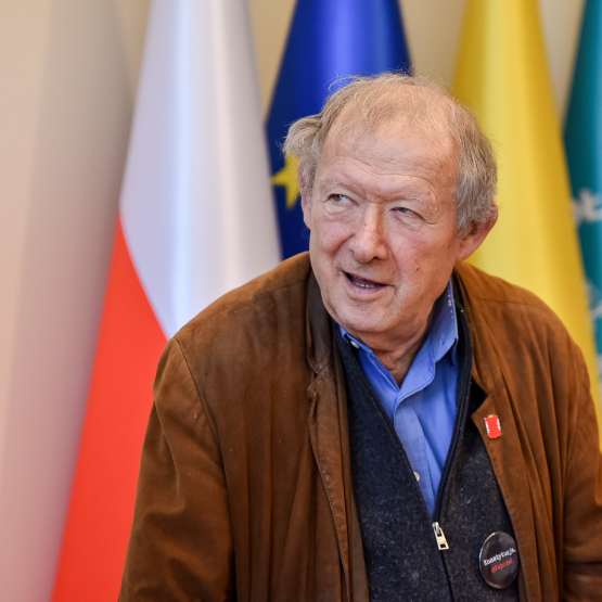 mężczyzna na tle flagi polskiej, unijnej, Warszawy i SGH