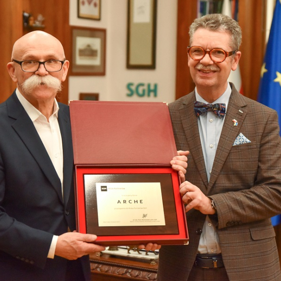 dwóch mężczyzn trzyma w rękach mosiężną tabliczkę informującą o przyjęciu firmy Arche do Klubu Partnerów SGH