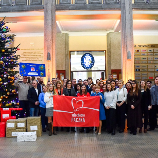 kilkanaście osób pozuje do zdjęcia przy dużej choince i prezentach 