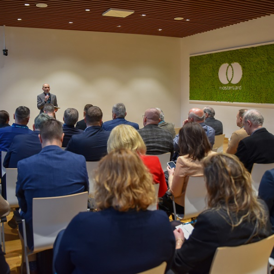 zdjęcie z sali wypełnionej ludźmi, gdzie odbywa się konferencja; jeden mężczyzna przemawia 