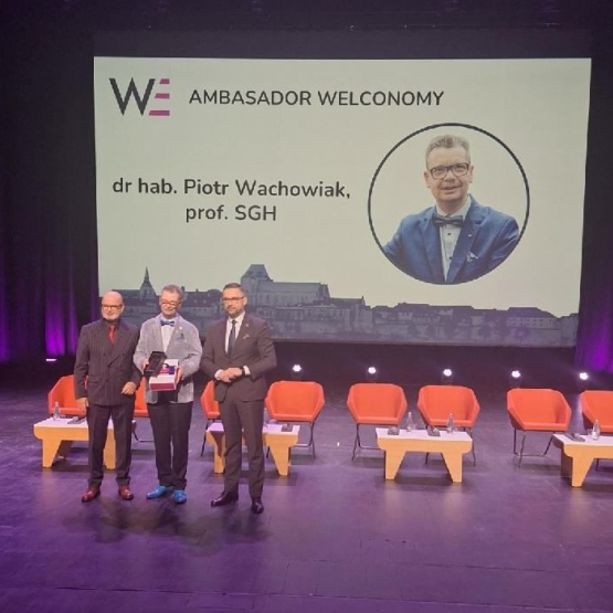 trzech mężczyzn stoi na scenie, jeden odbiera nagrodę