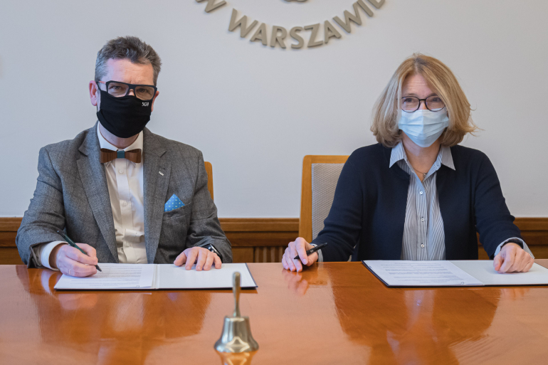 Rektor Piotr Wachowiak i dyrektor Maria Andrzejewska podpisują umowę o współpracę. Znajdują się w sali senatu. 