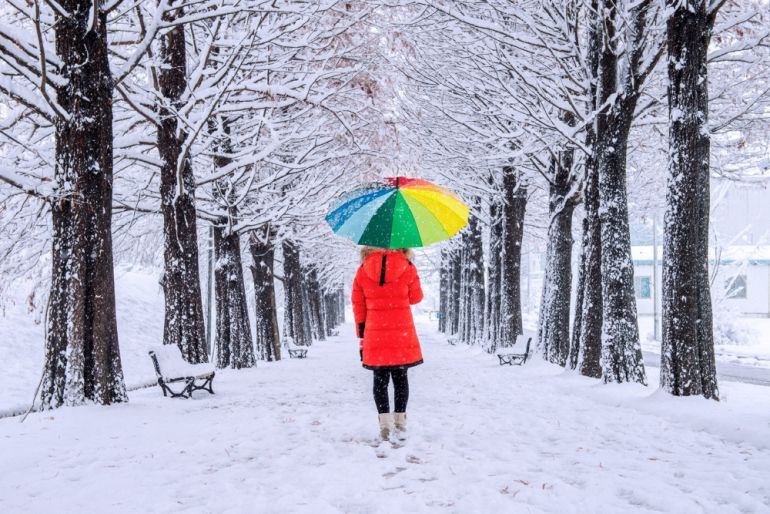 człowiek idący w śnieżnej alei z kolorowym parasolem