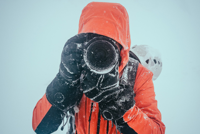 mężczyzna w czerwonej kurtce z aparatem fotograficznym