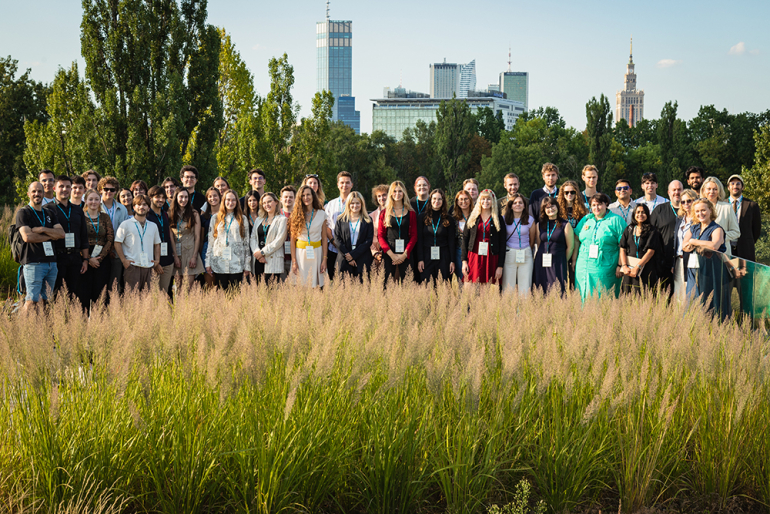 grupa pozujących osób na tle centrum Warszawy