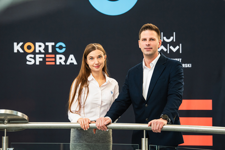 Kobieta i mężczyzna przy barierce na tle banera z napisem Kortosfera