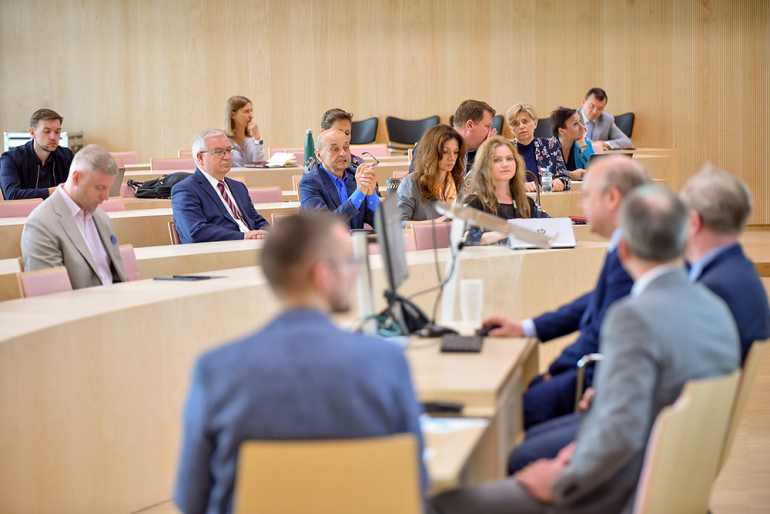 Sala wykładowa, grono słuchaczy patrzących na prelegentów 