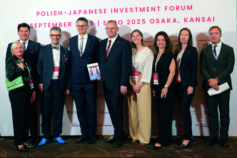 Dziewięć osób w oficjalnych strojach na tle baneru polsko-japońskiego forum inwestycyjnego
