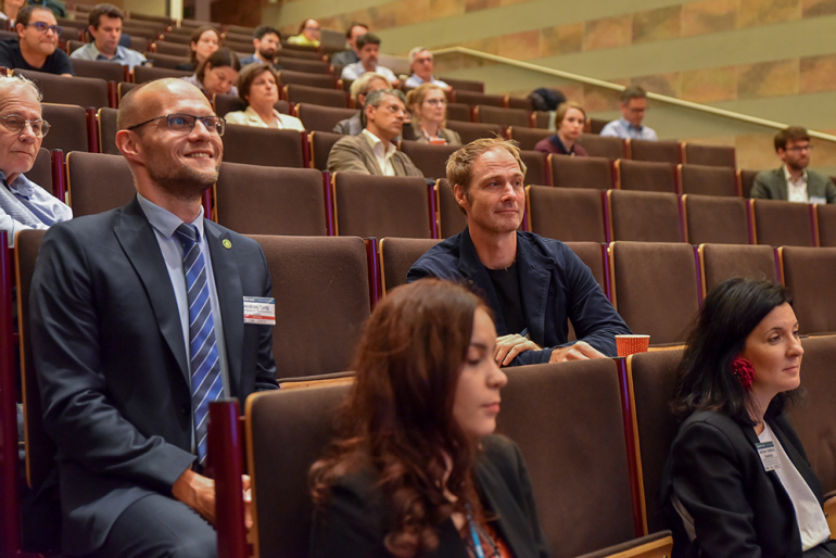 ludzie siedzący w ławkach w auli I budynku C