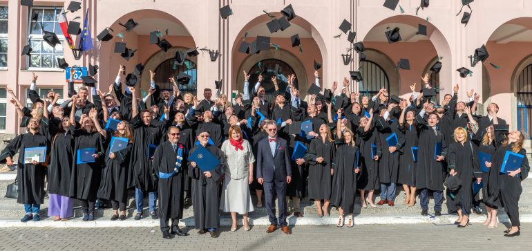 grupa ludzi zgromadzonych przed budynkiem głównym SGH, podrzucających birety