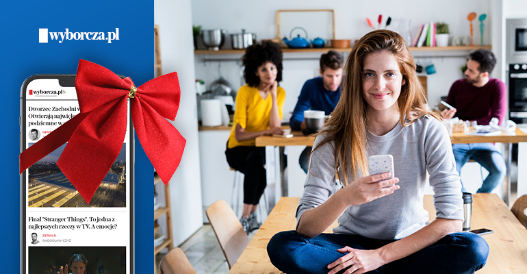 na pierwszym planie kobieta trzymająca komórkę, obok telefon komórkowy z czerwona kokardą