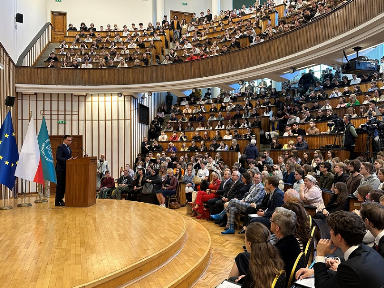 aula pełna studentów i wykładowców; na scenie przemawia mężczyzna