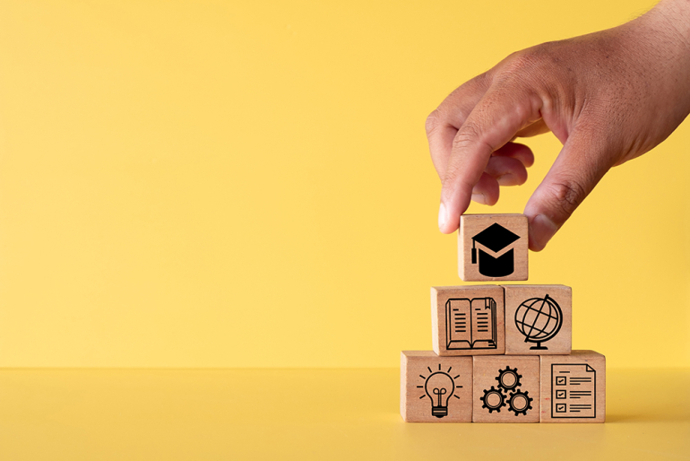 na żółtym tle dłoń układająca klocki z symbolami