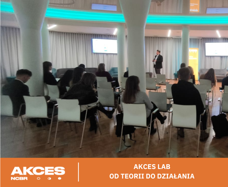 zdjęcie grupy osób na sali na dole pomarańczowy pasek z logami