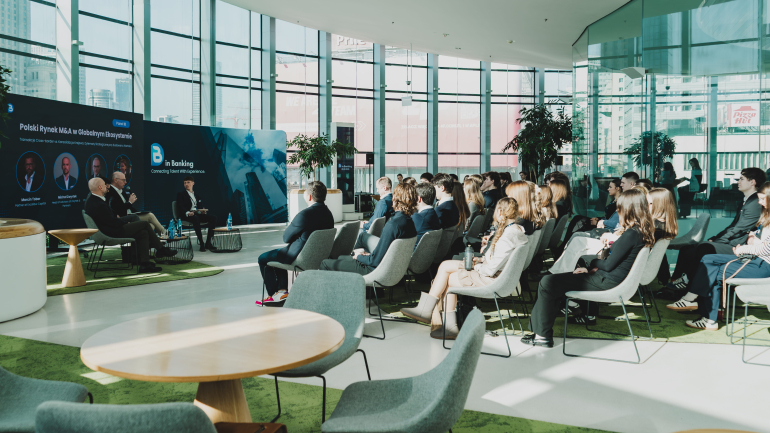 zdjecie pokazujące studentów na oszklonej sali i kilku prelegentów rozmawiających ze sobą podczas panelu dyskusyjnego
