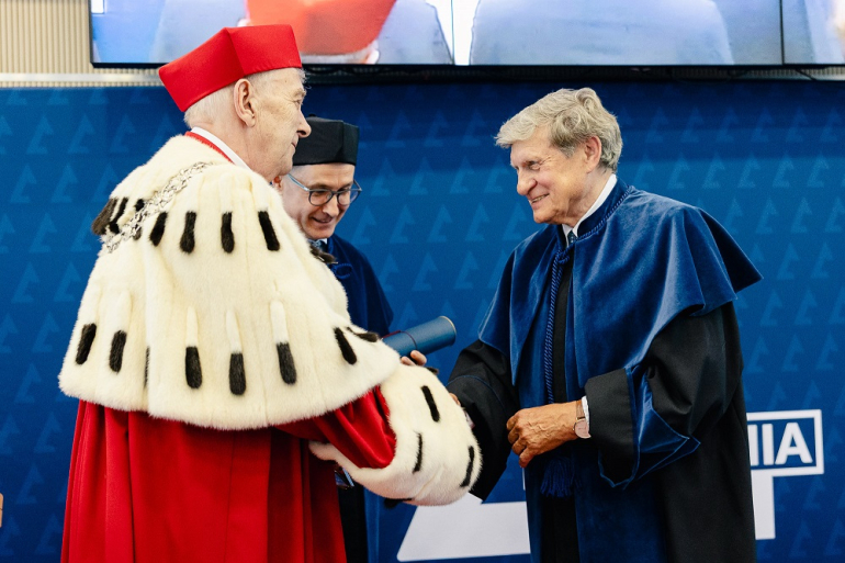 dwóch mężczyzn w togach; jeden w todze rektorskiej składa gratulacje drugiemu w todze doktora honoris causa