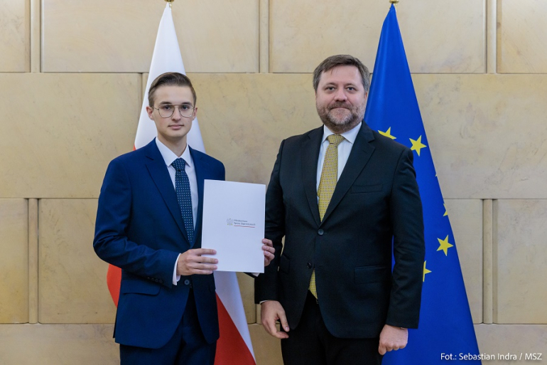 dwóch mężczyzn w garniturach na tle flagi Polski i UE