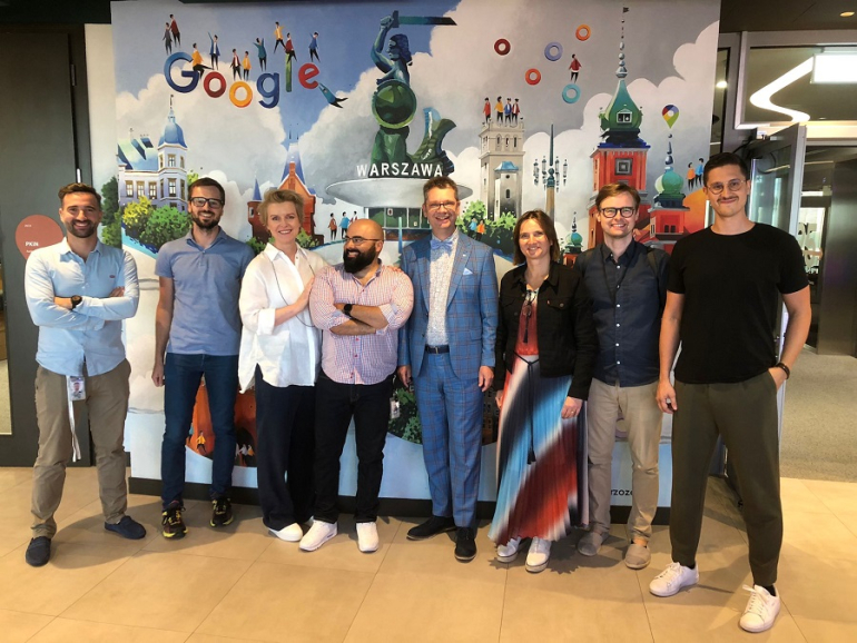 grupa osób stoi przed ścianą z napisem Google