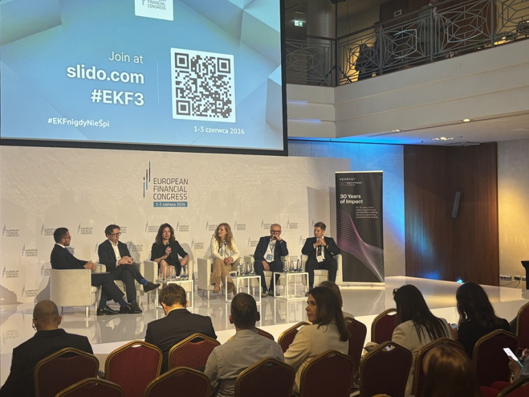 kilka osób dyskutuje na panelu, widać też ludzi siedzących na widowni