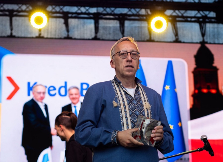mężczyzna w ludowej koszuli trzyma statuetkę na scenie