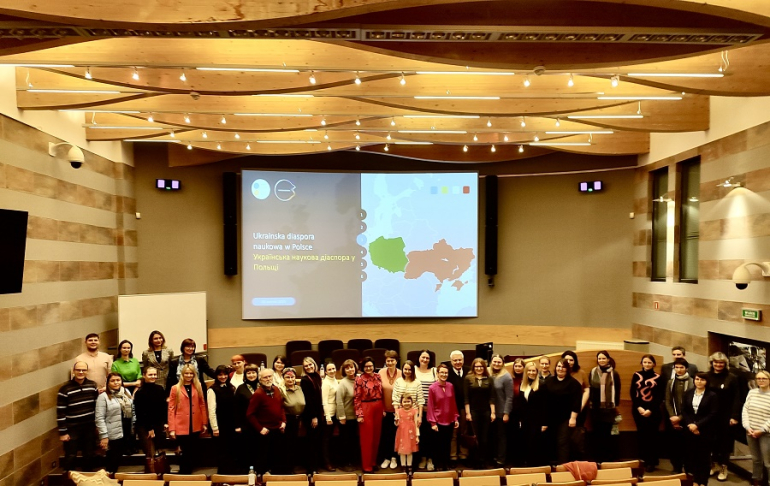 grupa osób stoi w jednej z sal wykładowych; za nimi ekran informujacy o spotkaniu Ukraińskiej diaspory naukowej w Polsce; napis po polsku i ukraińsku