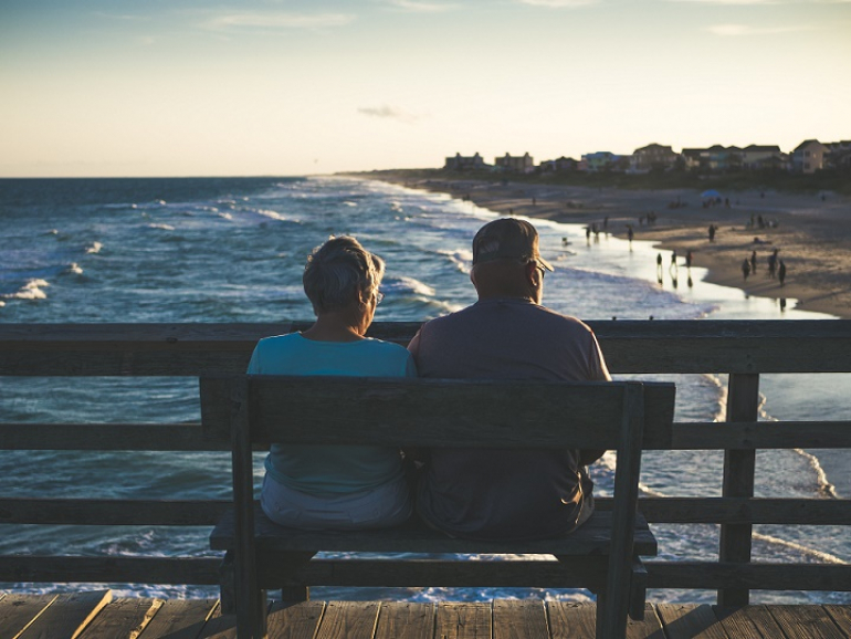 dwoje starszych ludzi siedzi na ławce na molo i spogląda w morze