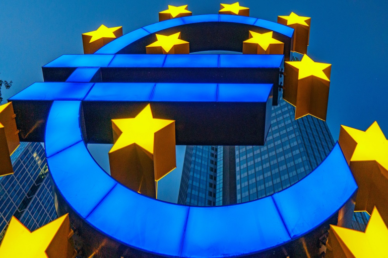niebieski znak euro i żółte gwiazdki na tle wieżowców