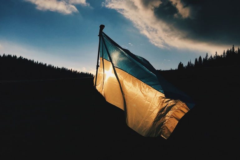 ukraińska flaga powiewająca na wietrze; w tle las i zachmurzone niebo