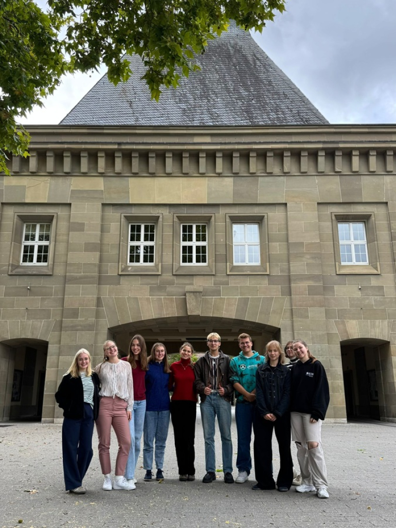 grupa młodych osób pozuje do zdjęcia przed budynkiem uniwersytetu