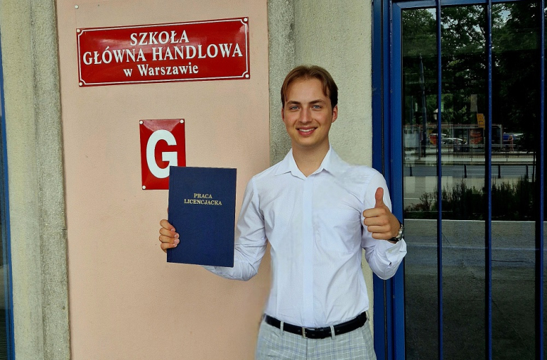 na zdjęciu Paweł Wróblewski z pracą dyplomową na tle budynku SGH