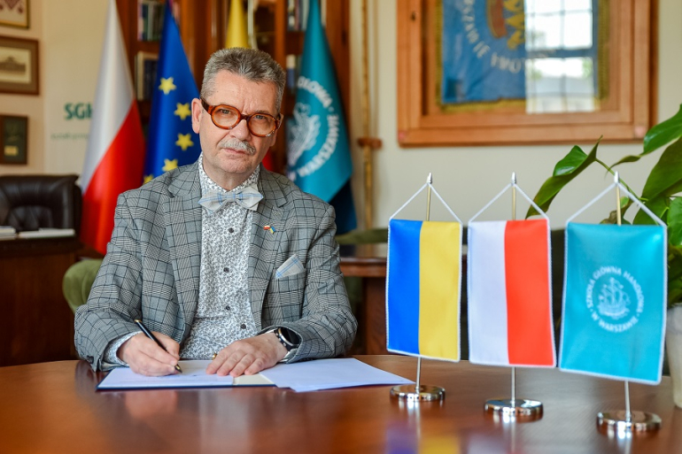 mężczyzna podpisuje dokumenty, obok proporczyki z flagą Ukrainy, Polski i SGH