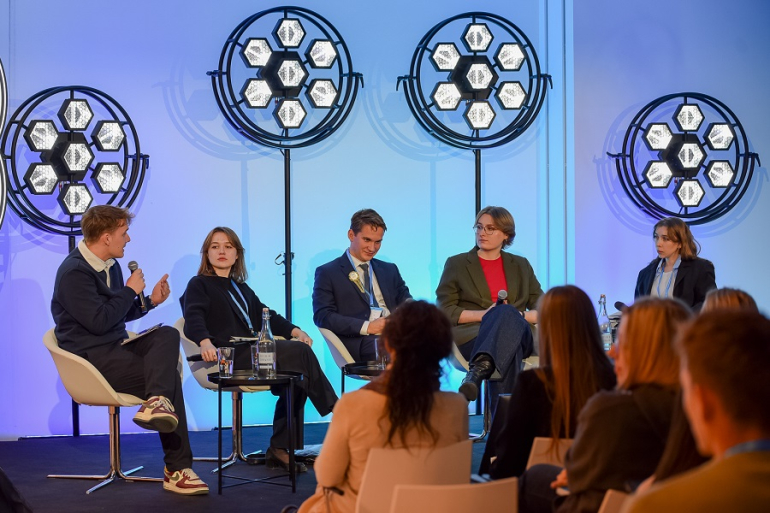 czworo młodych studentów rozmawia na panelu; z tyłu światła