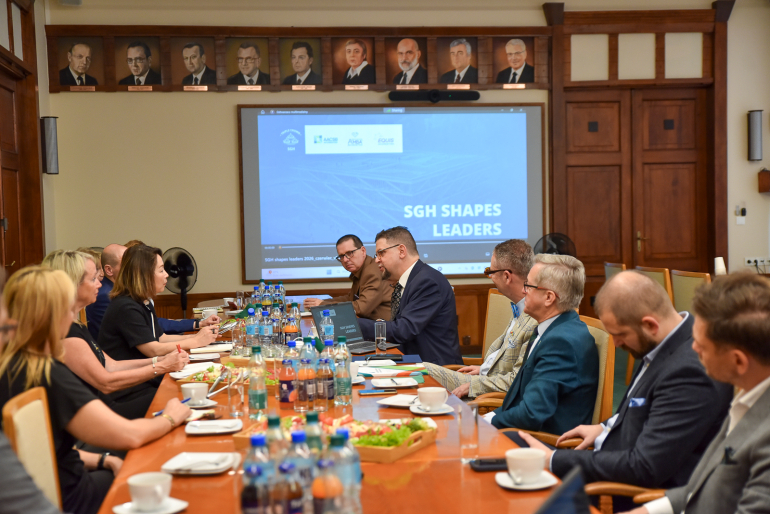 kilkanaście osób rozmawia przy stole konferencyjnym, w tle wyświetlana prezentacja