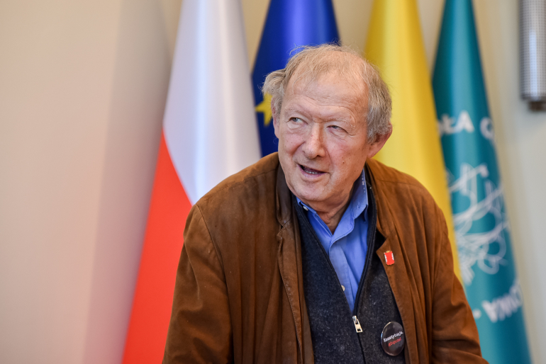 mężczyzna na tle flagi polskiej, unijnej, Warszawy i SGH