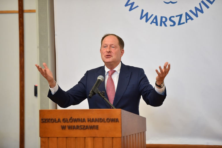 mężczyzna z rozłożonymi rękami przemawia zza mównicy