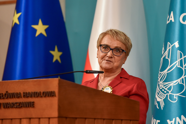 zdjęcie przemawiającej kobiet, z lewej strony flaga Polski